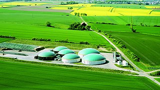 Luftaufnahme eines grünen Feldes mit sechs grünen Kuppeln der Biomethananlage Willingshausen