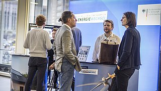 Mehrere Personen stehen an einem Messestand mit dem Schriftzug 'ENERGIE WECHSEL' und einem Bild von Windkraftanlagen