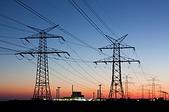 Elektrizitätsmasten vor einem malerischen Sonnenuntergang, der die Landschaft in sanfte Töne taucht.