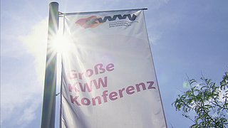 Fahne mit der Aufschrift 'Große KWW Konferenz' vor blauem Himmel und Sonne