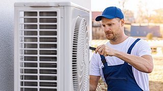 Ein Handwerker, der an einer Wärmepumpe arbeitet, die neben einem Haus installiert ist.