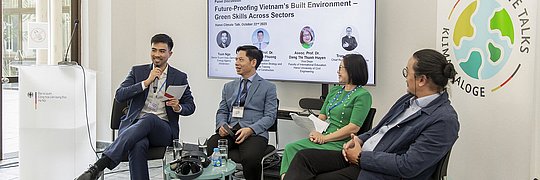 Vier Personen sitzen vor einem großen Bildschirm, dort ist zu lesen: "Future-Proofing Vietnam's Build Environment - Greven Skills Across Sektors". Sie diskurtieren. Die Teilnehmer von links nach rechts: Tun Ngo, Seniorexperte der Deutschen Energieagentur (dena), Assoc. Prof. Dr. Nguyen Vu Phuong, Vice President, Academy of Construction Strategy and Cadres Training, Ministry of Construction, Associate Prof. Dr. Dang Thi Thanh Huyen, Vice Dean, Faculty of International Education, Hanoi University of Civil Engineering, Mr. Tran Cong Duc, Chief Representative Vietnam, gmp Architects