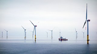 Mehrere Windkraftanlagen mit gelben Fundamenten stehen im Wasser, ein Schiff ist zwischen den Turbinen sichtbar.