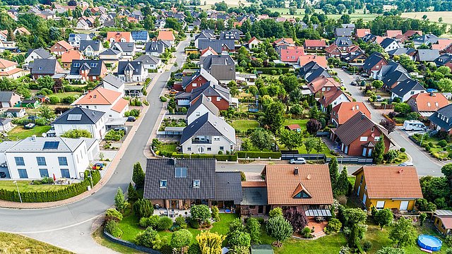 Luftaufnahme eines Wohngebiets mit Einfamilienhäusern, Gärten und Straßen in einer grünen Umgebung.