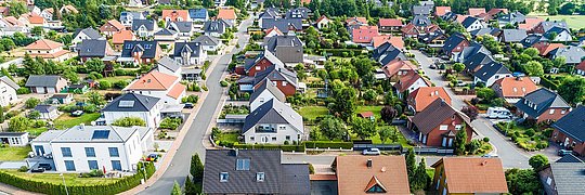 Luftaufnahme eines Wohngebiets mit Einfamilienhäusern, Gärten und Straßen in einer grünen Umgebung.