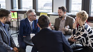 Eine Gruppe von fümf Personen sitzt auf Stühlen in einem Kreis und diskutiert