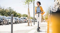 Eine glückliche junge Frau mit Kopfhörern fährt E-Scooter in der Stadt.
