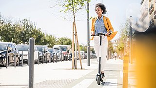 Eine glückliche junge Frau mit Kopfhörern fährt E-Scooter in der Stadt.