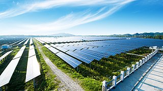 Photovoltaikmodule reflektieren Sonnenlicht, darüber Himmel mit Wolken
