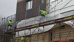 Personen auf einem Gerüst vor einem Gebäude, das mit Planen abgehängt ist