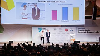 Auf der Bühne der Preisverleihung 2017 sind die Moderatorin und ein Laudator zu sehen.
