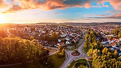 Luftaufnahme einer Vorstadt mit Wohnhäusern, Straßen und einem Kreisverkehr bei Sonnenuntergang