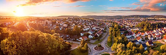 Luftaufnahme einer Vorstadt mit Wohnhäusern, Straßen und einem Kreisverkehr bei Sonnenuntergang