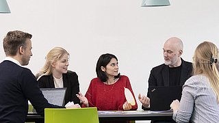 Eine Gruppe von Menschen sitzt um einen Tisch herum und arbeitet mit Laptops.