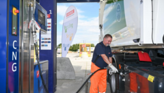 Mann in orangefarbener Arbeitskleidung betankt Lkw mit CNG an einer blauen Zapfsäule
