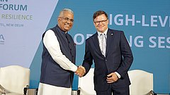 Bundesumweltminister Carsten Schneider und sein indischer Amtskollege Bhupender Yadav geben sich auf der Bühne des 4. Deutsch-Indischen Umweltforums die Hand. Im Hintergrund ist eine Leinwand sichtbar.