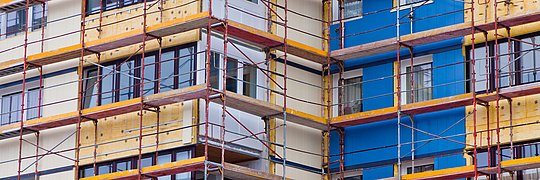 Fassade eines mehrstöckigen Gebäudes mit Gerüst und teilweise isolierter Außenwand