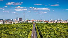 Das Bild zeigt eine Panoramaansicht von Berlin mit üppigem Grün im Vordergrund.