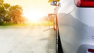 Elektroauto wird an Ladestation aufgeladen, Sonnenlicht im Hintergrund