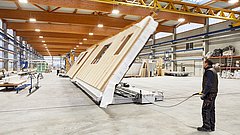 Mann bedient Maschine, die große vorgefertigte Wand in moderner Fabrikhalle hebt