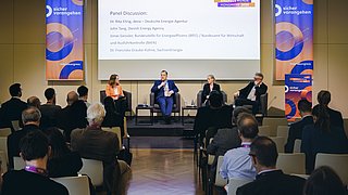 Podiumsdiskussion mit vier Personen auf einer Bühne vor Publikum und zwei großen Bannern mit dem Schriftzug "sicher vorangehen"