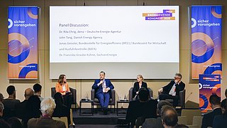 Podiumsdiskussion mit vier Personen auf einer Bühne vor Publikum und zwei großen Bannern mit dem Schriftzug "sicher vorangehen"