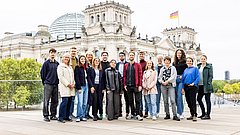 Gruppe von 17 Personen steht vor dem Reichstagsgebäude in Berlin mit zwei deutschen Flaggen auf den Türmen
