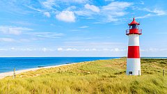 Leuchtturm mit roten und weißen Streifen auf einer Dünenlandschaft am Meer unter blauem Himmel