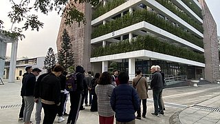 Gruppe von vietnamesischen Studierenden steht im Halbkreis vor einem modernen, mehrstöckigen Gebäude. Das Gebäude hat eine helle, horizontale Fassade mit integrierter Vegetation.