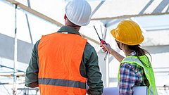 Ingenieure mit Sicherheitswesten und Bauhelmen halten eine Besprechung in einer Industriehalle ab.