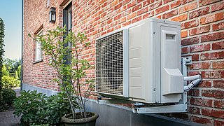 Außenwand eines Backsteinhauses mit einer an der Wand montierten Klimaanlage und einem Blumentopf mit grünem Strauch davor