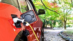 Rotes Elektroauto wird im Grünen über ein Ladekabel aufgeladen.