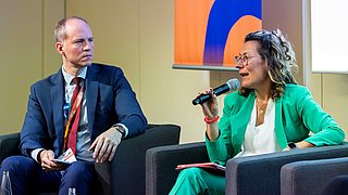 Michaela Steinhauser und Michel Durieux sitzen auf dem Podium und diskutieren. 