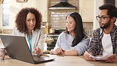 3 Personen an einem Tisch, auf dem ein Computer steht