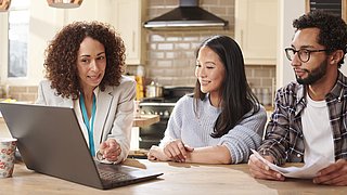 3 Personen an einem Tisch, auf dem ein Computer steht