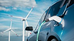 Ein Elektroauto mit einem Ladekabel, das an die Ladebuchse angeschlossen ist. Im Hintergrund sind Windkraftanlagen zu sehen.