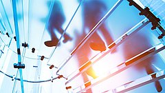 Silhouetten von Personen, die auf transparenten, horizontalen Ebenen gehen, mit Lichtreflexionen im Hintergrund.