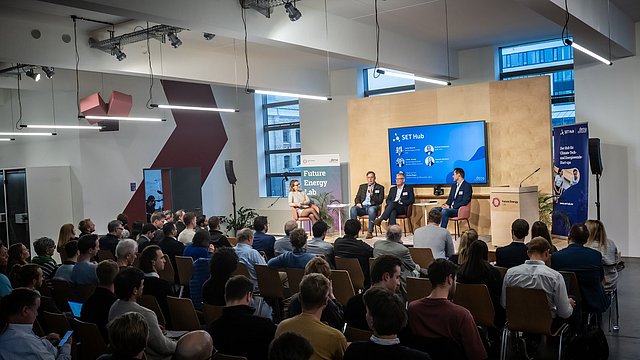 Panel-Diskussion im Future Energy Lab: Vier Personen sitzen auf der Bühne und diskutieren vor einem Publikum in einem modernen, gut beleuchteten Veranstaltungsraum. Im Hintergrund sind ein großer Bildschirm mit der Aufschrift 'SET Hub' und Banner mit den Logos von 'Future Energy Lab' und 'dena' zu sehen.