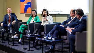 Fünf Personen sitzen auf einem Podium und diskutieren miteinander.