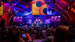 Große Veranstaltung in einer beleuchteten Halle: Publikum blickt auf eine farbenfrohe Bühne mit Show-Elementen, Screens und dem Schriftzug „SET the future“.