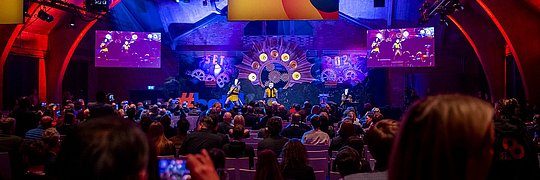 Große Veranstaltung in einer beleuchteten Halle: Publikum blickt auf eine farbenfrohe Bühne mit Show-Elementen, Screens und dem Schriftzug „SET the future“.