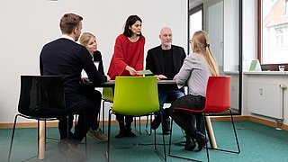 Fünf Mitarbeitende der dena sitzen gemeinsam im Gespräch an einem Tisch.