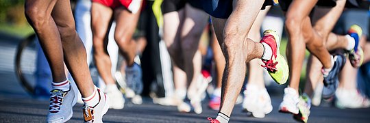 Marathonlaufende in kurzen Sporthosen auf asphaltier-tem Weg. Bildausschnitt ohne Oberkörper