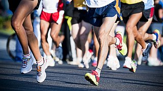 Marathonlaufende in kurzen Sporthosen auf asphaltier-tem Weg. Bildausschnitt ohne Oberkörper