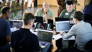 Teilnehmende der EnerCise Cyberübung III am 23.06.2026 im Future Energy Lab der dena arbeiten in einer offenen Büroumgebung mit Laptops und Notizen. Die Übung trainiert OT-Incident-Response und bereichsübergreifende Zusammenarbeit für Verteilnetzbetreiber.