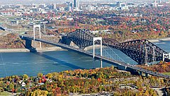 Eine Brücke, die über einen Fluss führt, umgeben von Bäumen und klarem Himmel.
