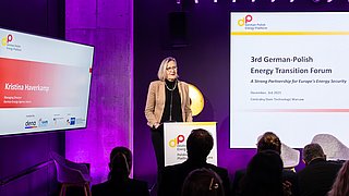 Frau steht am Rednerpult vor Publikum in einem Konferenzraum mit zwei großen Bildschirmen, einer zeigt den Titel '3rd German-Polish Energy Transition Forum' und der andere den Namen 'Kristina Haverkamp'