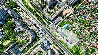 Luftaufnahme einer Stadt mit hohen Wohngebäuden, breiten Straßen und grünen Flächen.