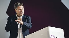 Robert Habeck in schwarzem Anzug mit Mikrofon, steht an einem weißen Rednerpult mit dem Logo 'Future Energy Lab'.