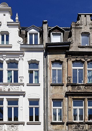 Zweistöckige Fassade mit Giebel, links frisch renoviert in Weiß, rechts unrenoviert mit sichtbarem Verwitterungsschmutz.